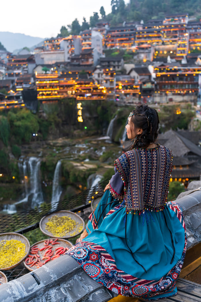 Mujer China que admira la vista de la ciudad de Lijiang. Al fondo se ve la ciudad que esta sobre unas cascadas.